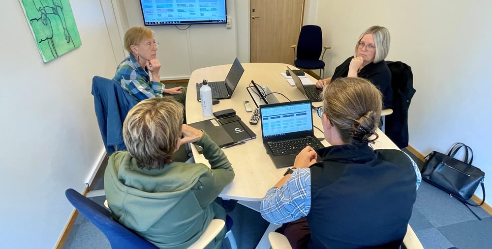 Fyra personer sitter kring ett runt bord. De har datorer framför sig.