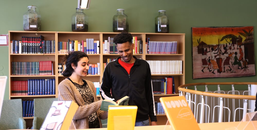 Två kursdeltagare står i ett bibliotek och tittar ned i en bok