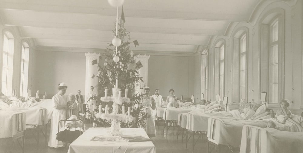 Svart-vit bild med en ny sjukhussal från 1900-talet. Dekorerad med julgran, barn i sängar och vårdpersonal i rummet