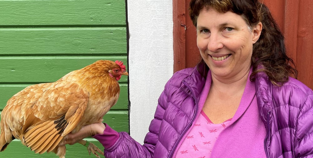 Linn Vadfors, som driver projektet med hönshållning, håller i en höna i sin högra hand.