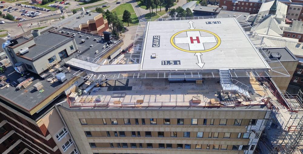 Bilden visar den nya helikopterplattan på taket av hus 60. Helikopterplattan är fortfarande en byggarbetsplats. Bilden visar också en del av den ny tillbyggnaden av 6 våningar och den nya fasaden på den södra sidan av byggnaden. 