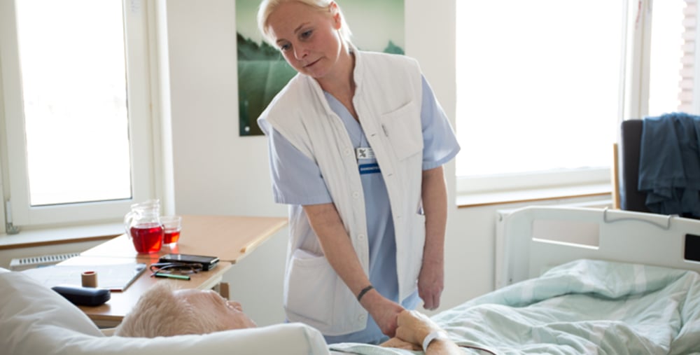 En person i en sjukhussäng får hjälp av en sjuksköterska.