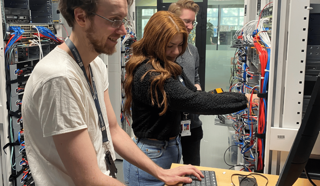 Tre personer arbetar vid servrar och kablage i en datahall.