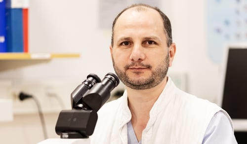 En man sitter vid ett bord framför ett mikroskop.