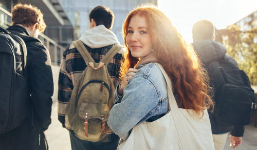Female student glancing back while going for a class in college. Girl walking with friends going for class in high school.