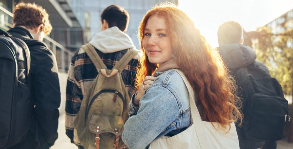 Female student glancing back while going for a class in college. Girl walking with friends going for class in high school.