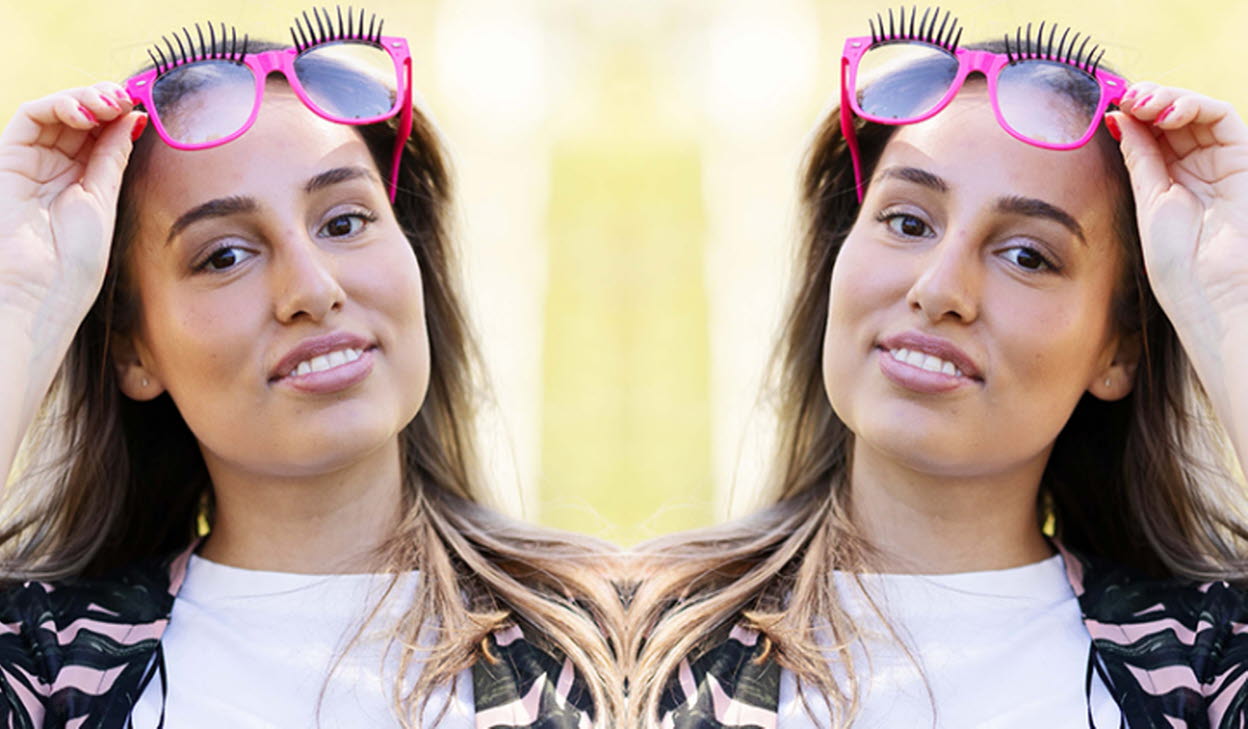 Person tittande in i kameran hållande ett par rosa solglasögon ovanför sitt huvud