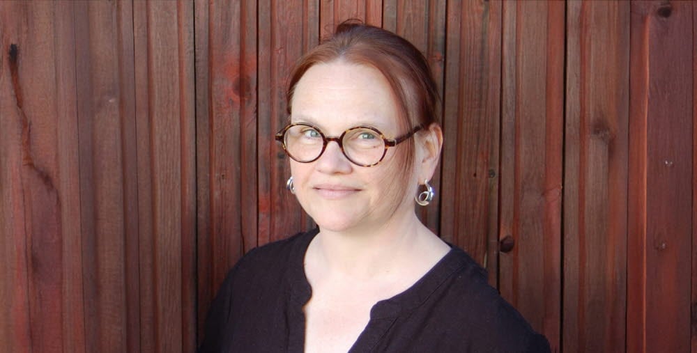 Porträtt av en person mot en träpanel i bakgrunden.