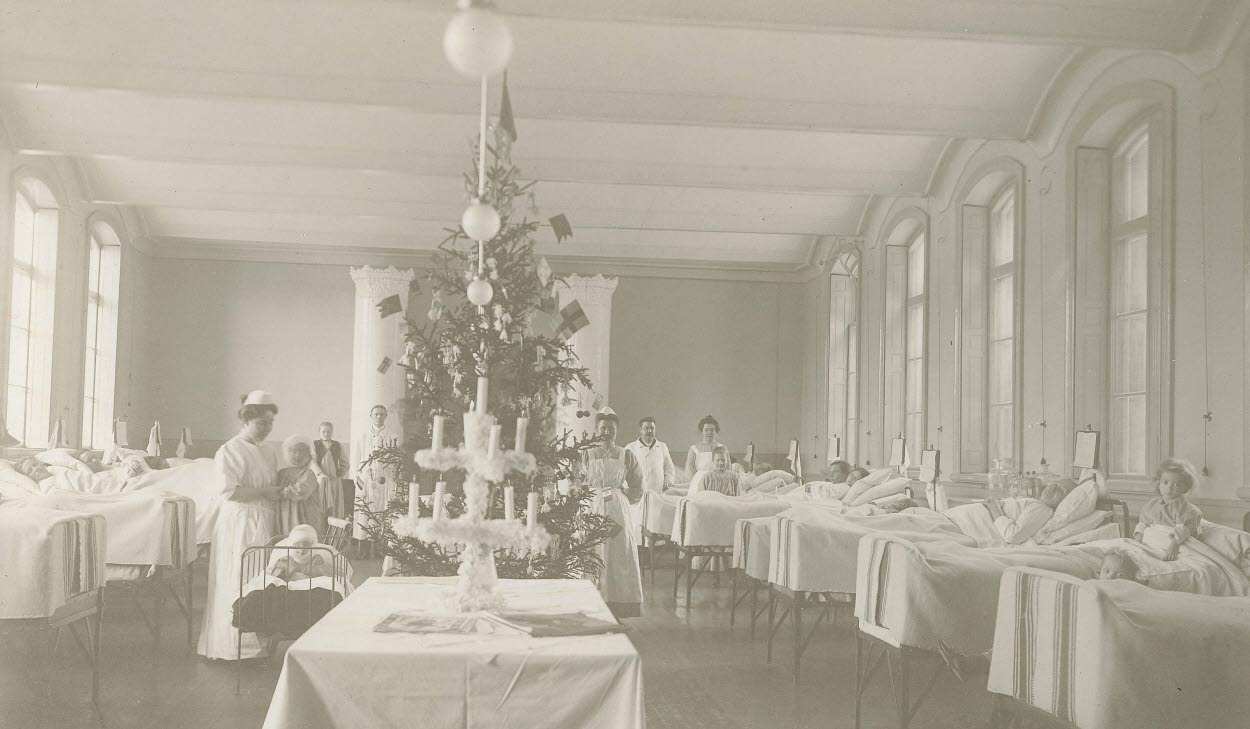 Svart-vit bild med en ny sjukhussal från 1900-talet. Dekorerad med julgran, barn i sängar och vårdpersonal i rummet