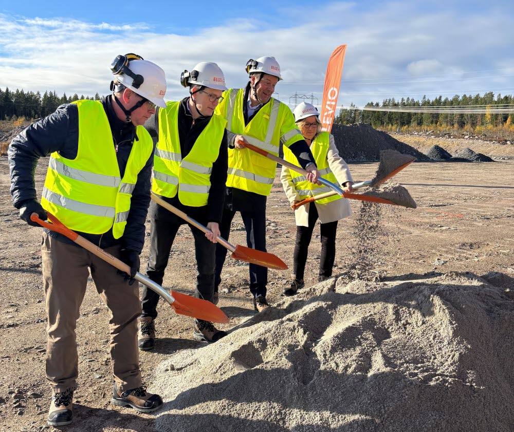 Fyra personer i bygghjälmar och reflexvästar tar första spadtaget med varsin spade på en byggarbetsplats.