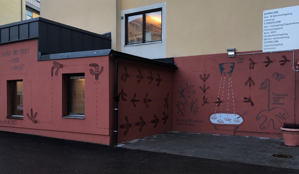 Väggmålning med växtmotiv och text pryder en husfasad vid en entré.