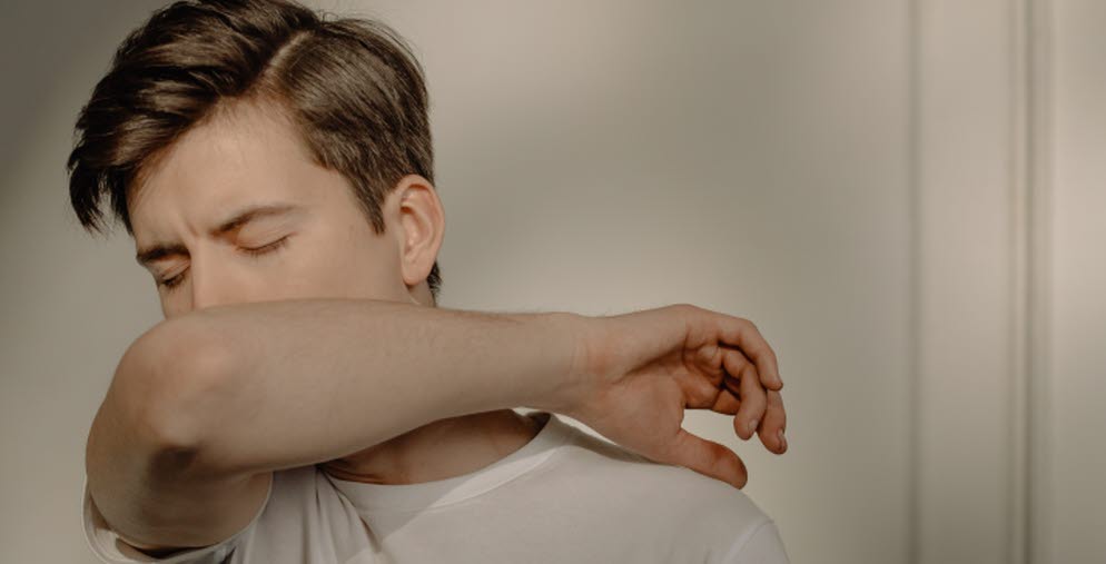 Person som verkar vara förkyld och nyser i armvecket.